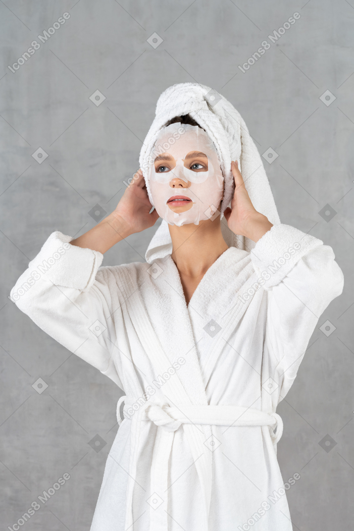 Woman in bathrobe with face mask on holding head