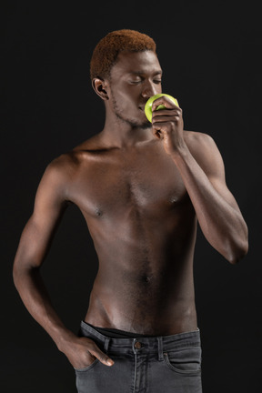 Close-up un hombre africano oliendo una manzana verde en la oscuridad