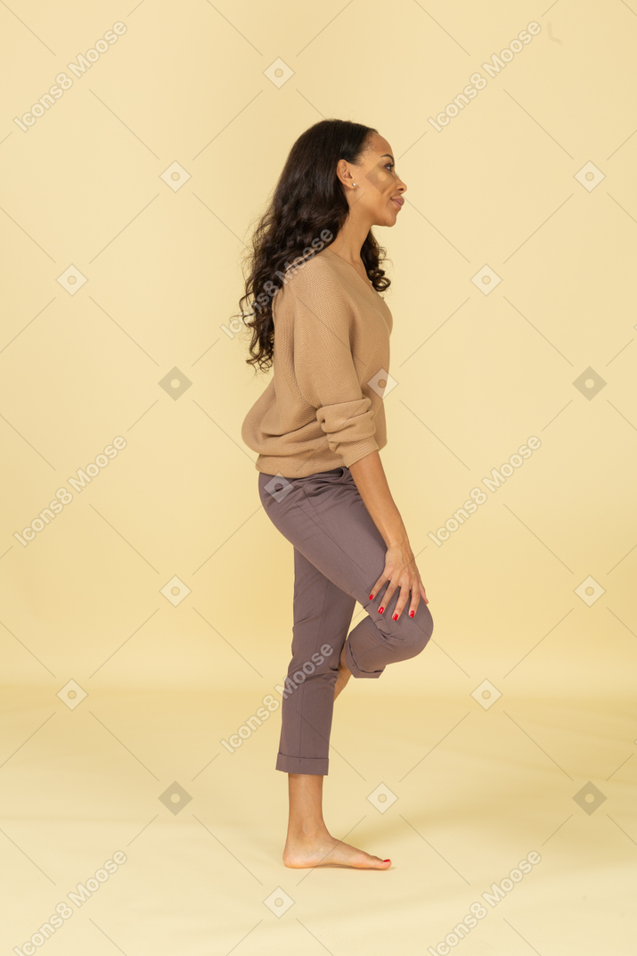 脚に手を置く退屈な若い浅黒い肌の女性の側面図