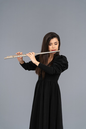 Front view of a serious young lady in black dress playing the flute