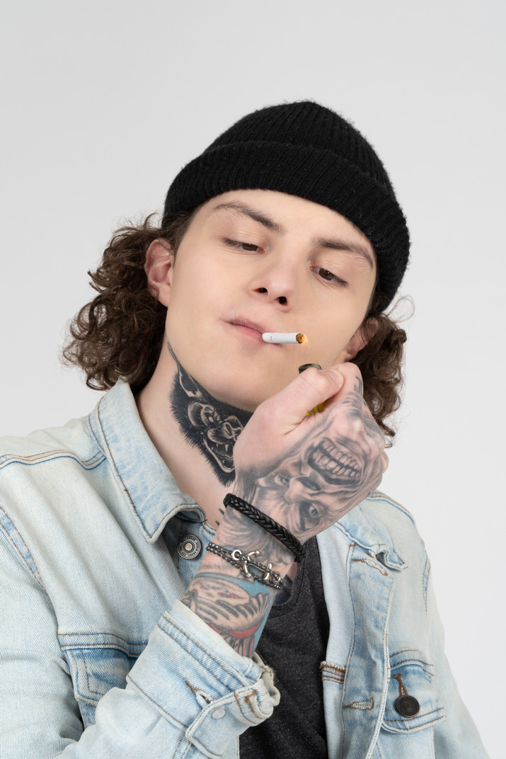 Young man with tattooed hands lighting a cigarette