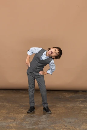 Front view of a boy in suit posing with hands on hips and showing tongue