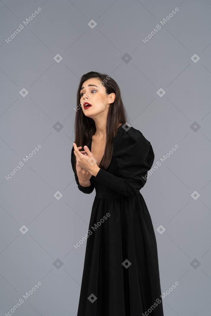 Вид в три четверти взволнованной жестикулирующей молодой женщины в черном платье