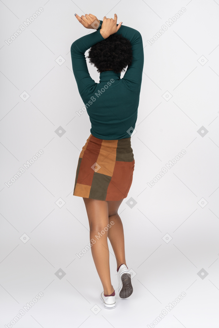 Adolescente de cabelos preto em pé volta para a câmera com as mãos levantadas