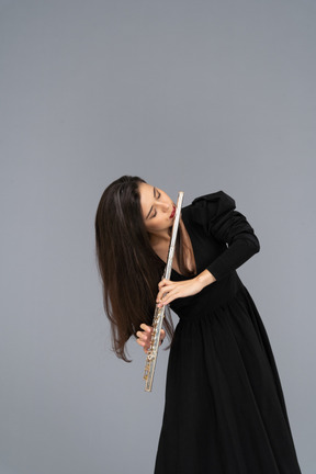 Front view of a serious young lady in black dress playing the flute