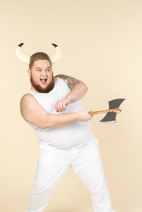 An emotional plus-sized man in white with a horned helmet on his head, holding a double-bladed axe