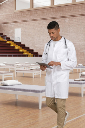 A male doctor in a white lab coat is looking at a tablet