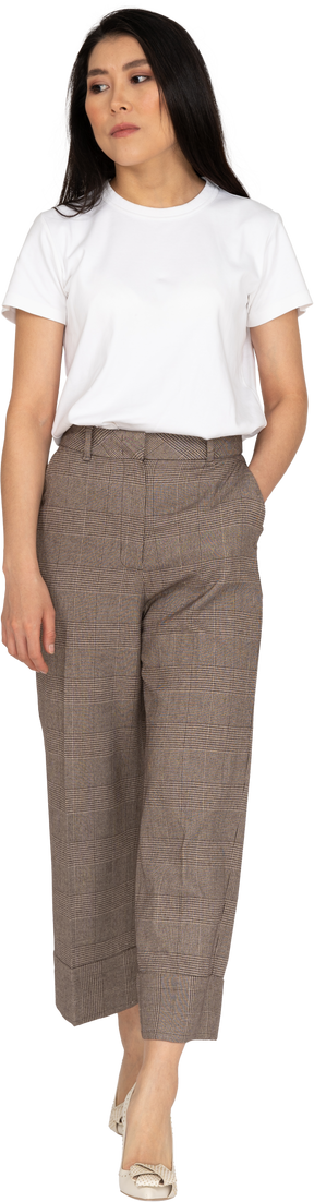 Vista frontale di una giovane donna annoiata a piedi in calzoni e t-shirt mettendo le mani in tasca