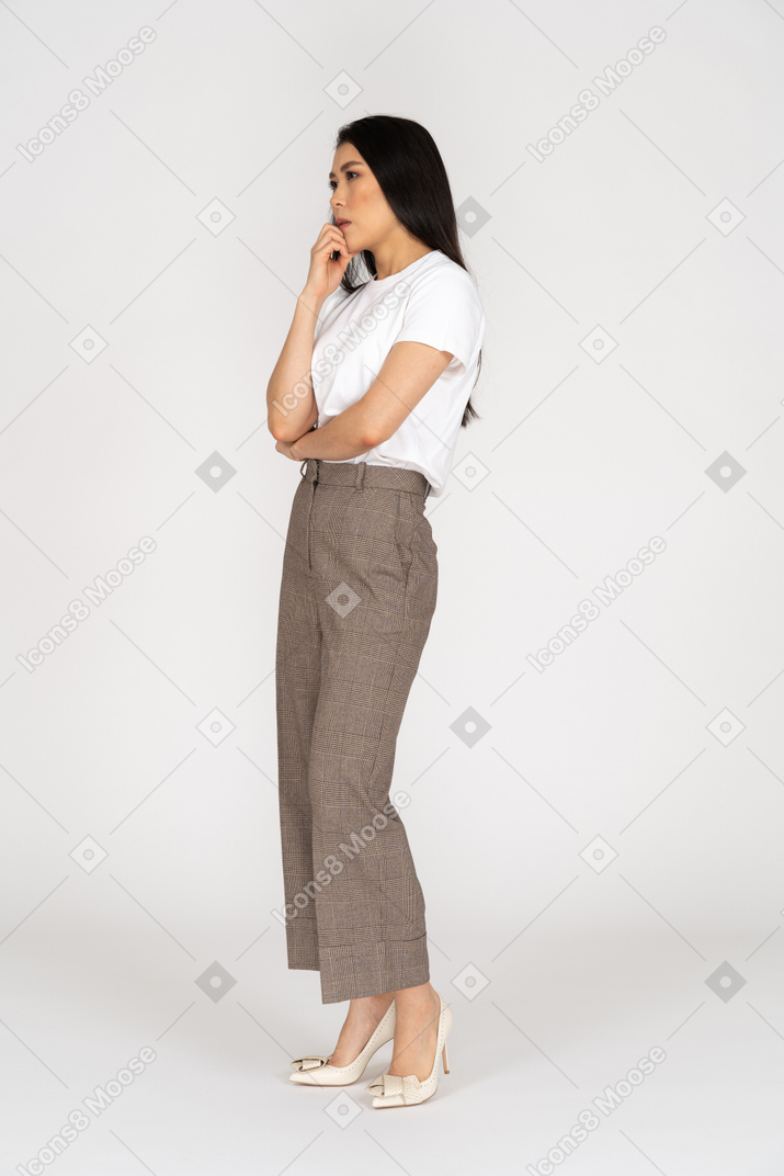 Three-quarter view of a thoughtful young lady in breeches and t-shirt touching chin