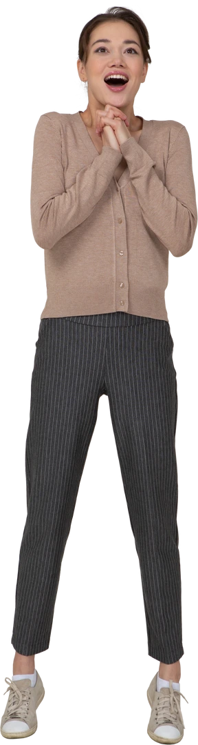 Front view of a delighted young lady in beige pullover holding hands together