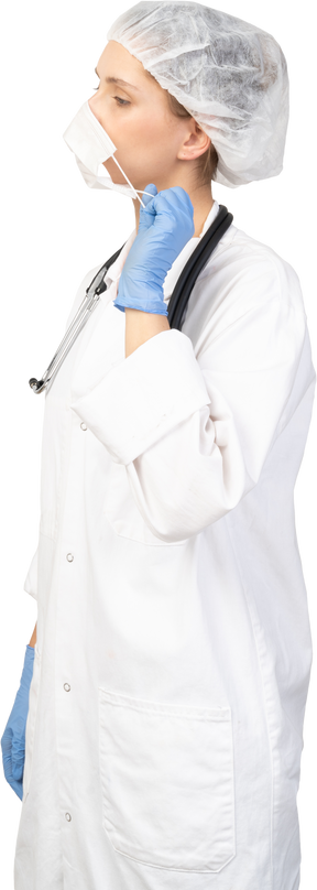 Вид в три четверти молодой женщины-врача, снимающей маску