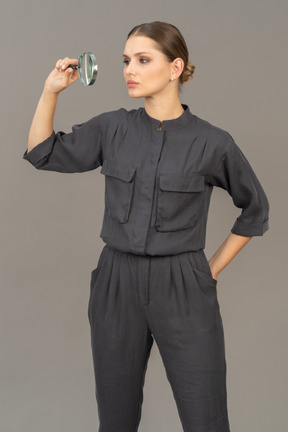 Front view of young woman in a jumpsuit holding a magnifying glass