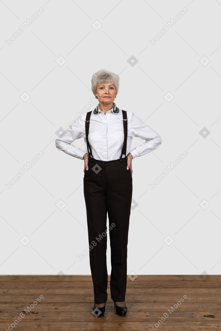 Comprimento total de uma mulher idosa em suspensórios colocando as mãos nos quadris