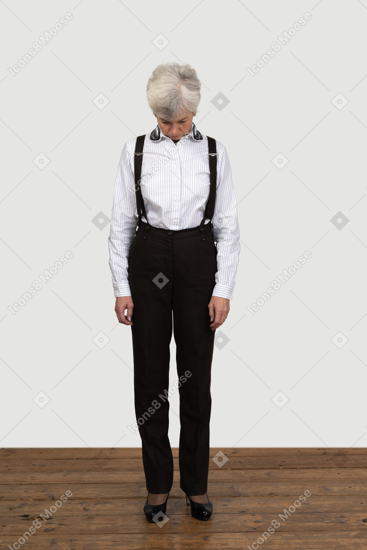 Vista frontal de una vieja mujer ofendida en ropa de oficina de pie todavía en el interior mirando a un lado