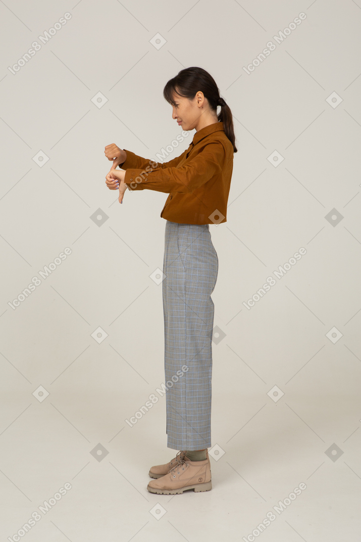 Side view of a young asian female in breeches and blouse showing thumbs down