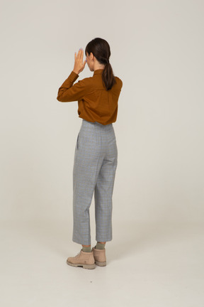 Three-quarter back view of a young asian female in breeches and blouse raising hands