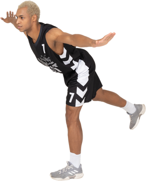 Dreiviertelansicht eines balancierenden jungen männlichen basketballspielers, der sich nach vorne lehnt und auf einem bein steht