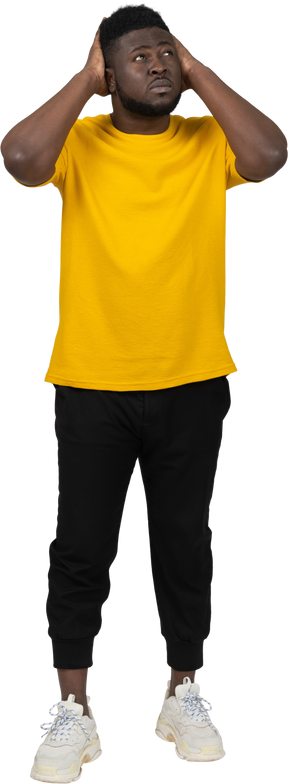 Vista frontal de um jovem de pele escura em uma camiseta amarela tocando a cabeça e olhando para cima
