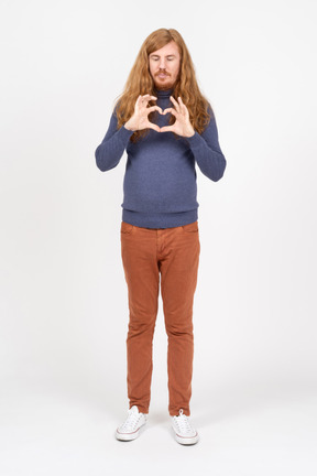 Front view of a young man in casual clothes making heart with fingers