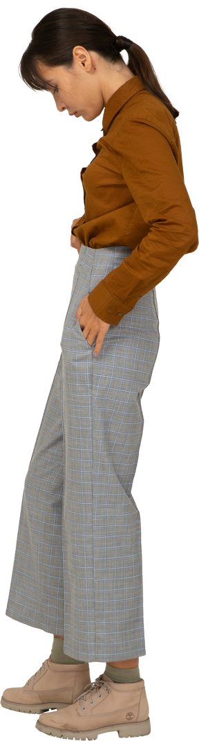 Vista lateral de uma jovem mulher asiática de calça e blusa colocando as mãos nos bolsos