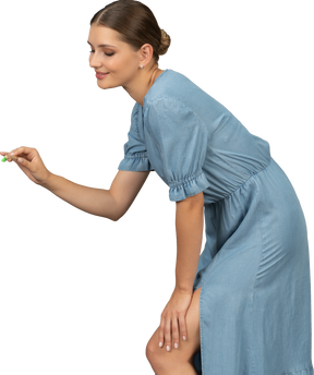 Vista laterale di una giovane donna in abito blu che tiene in mano uno spazzolino da denti e si sporge in avanti