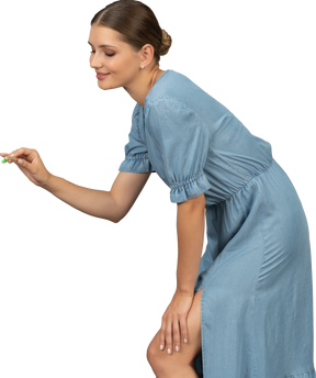 Side view of a young woman in blue dress holding toothbrush & leaning forward