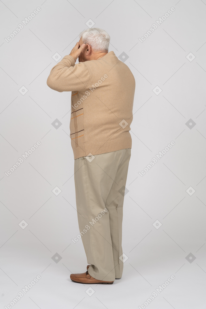 Side view of an old man in casual clothes covering eyes with hands