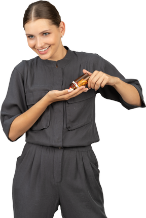 一个穿着连身衣的微笑年轻女子从罐子里倒药丸的前视图