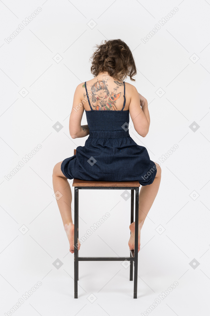 Young tattooed woman sitting on bar chair back to camera