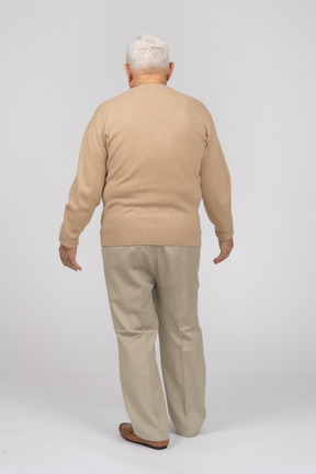Vue arrière d'un vieil homme en vêtements décontractés marchant avec les bras tendus
