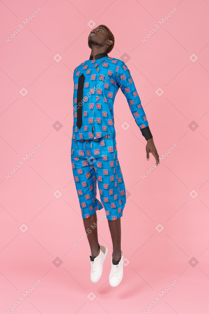 Black man in blue pajamas jumping on pink background