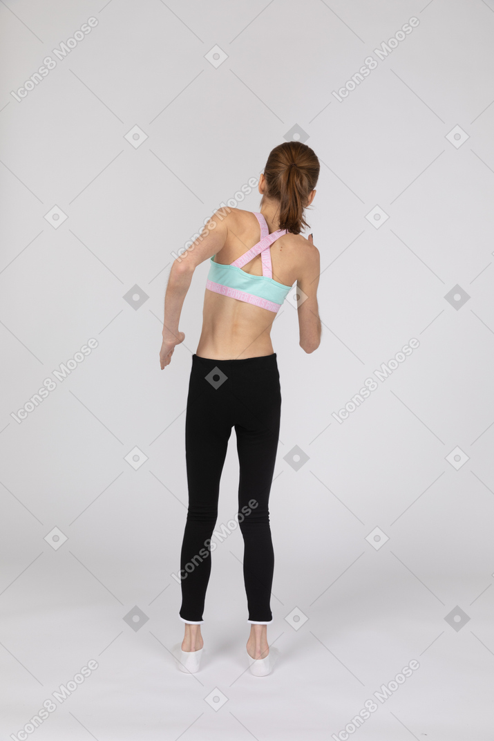 Vista traseira de uma adolescente em roupas esportivas inclinando-se para o lado em pé como um robô