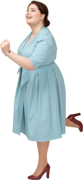 Женщина в синем платье балансирует на одной ноге, вид сбоку