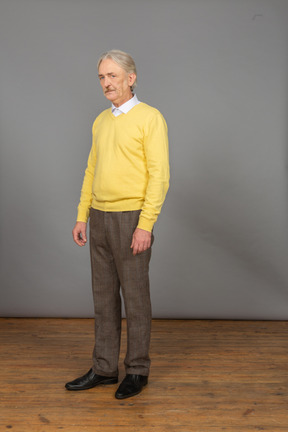 Three-quarter view of a displeased old man wearing yellow pullover and looking at camera