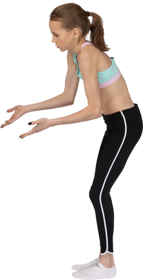 Vista lateral de uma adolescente em roupas esportivas apontando as mãos em algum lugar para baixo