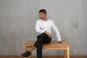 Well-dressed man sitting on a table with his head turned