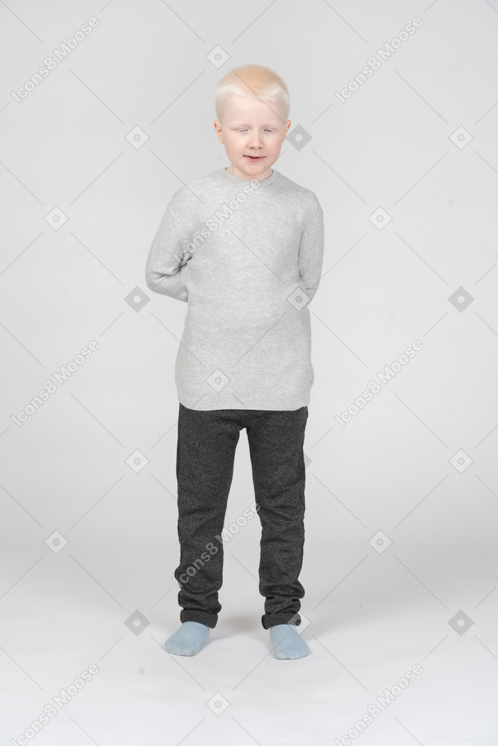 Front view of a kid boy with his eyes closed and hiding hands behind back