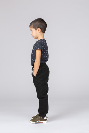 Vue latérale d'un garçon mignon posant avec les mains dans les poches