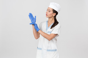 Attraktive krankenschwester in einem medizinischen gewand, das latexhandschuhe überzieht