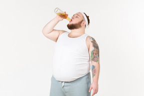 Um esportista gordo bebendo cerveja da garrafa