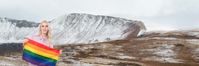 Person holding a rainbow flag on top of a snow covered mountain