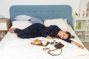 Front view of a laying in bed young lady having breakfast