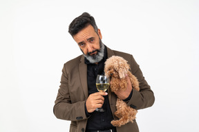 Homem maduro dando um gole de vinho para um cachorro que ele está segurando