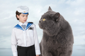 A boy in a sailor's uniform standing next to a big cat