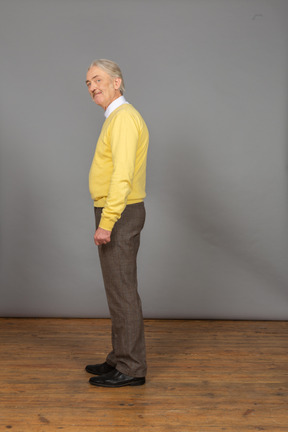 Seitenansicht eines alten fröhlichen mannes im gelben pullover, der sich bückt und kamera betrachtet