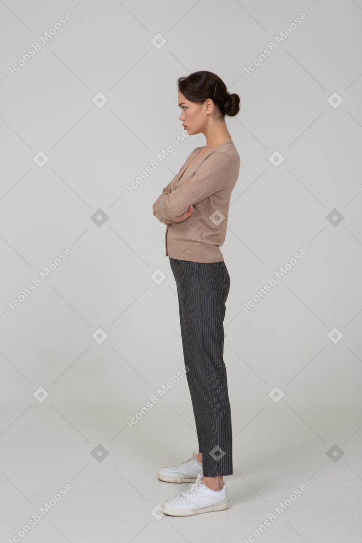 Vista lateral de uma jovem ofendida de pulôver e calças cruzando as mãos
