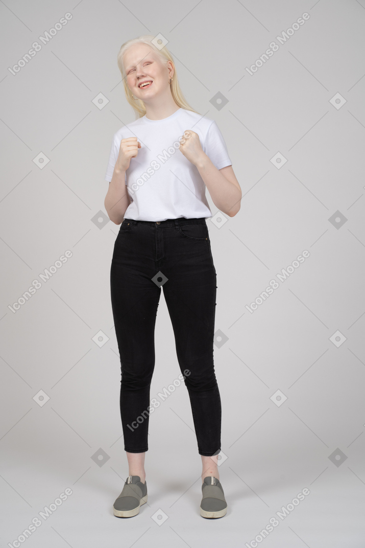 Улыбающаяся молодая женщина, стоящая со сжатыми кулаками