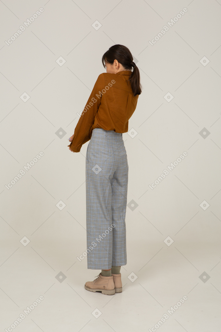 Three-quarter back view of a young asian female in breeches and blouse holding hands together and leaning back