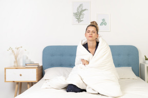 Vista frontal de uma jovem cansada de pijama enrolada em um cobertor e ficando na cama