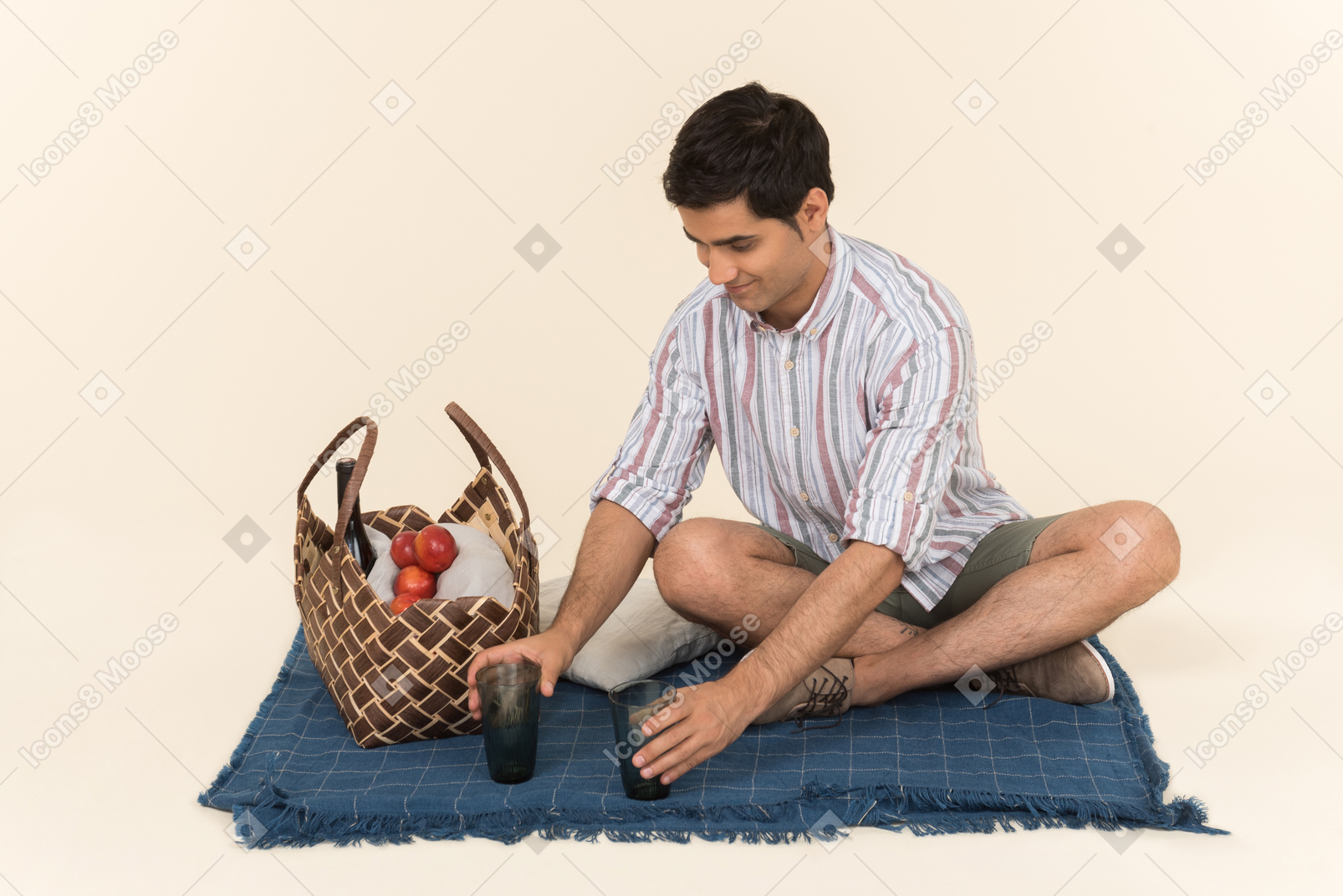 Young caucasian guy putting glasses on blue blanket for a picnic